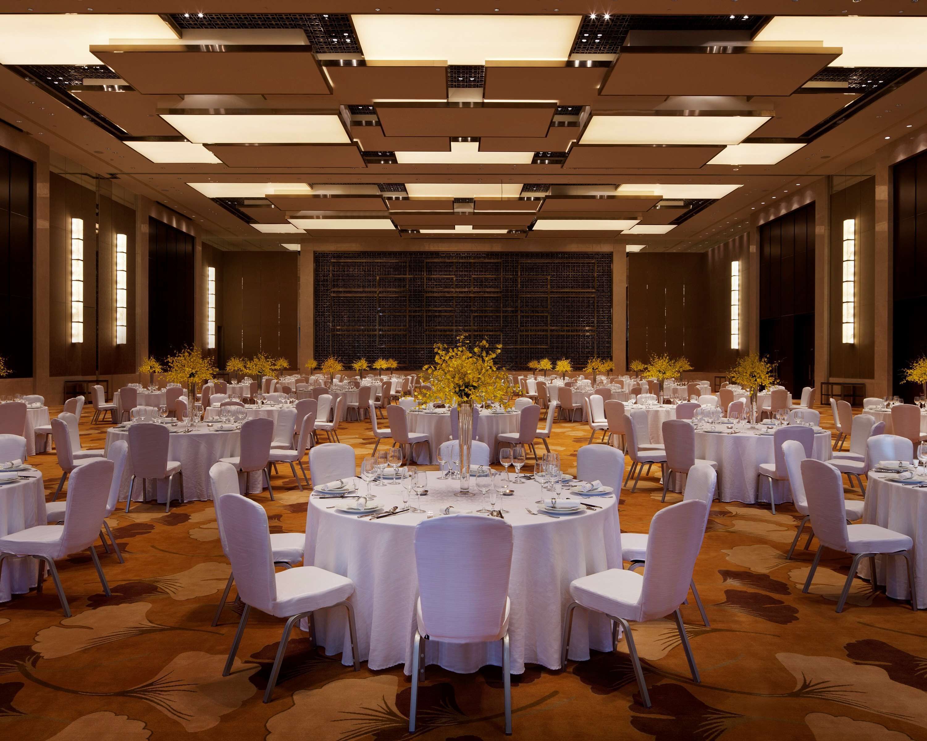 Un amplio salón de banquetes con mesas redondas dispuestas para cenar, sillas blancas y un arreglo floral en el centro.