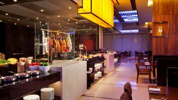 A modern restaurant with a central bar area, multiple dining tables, and a variety of food items displayed on the counter.