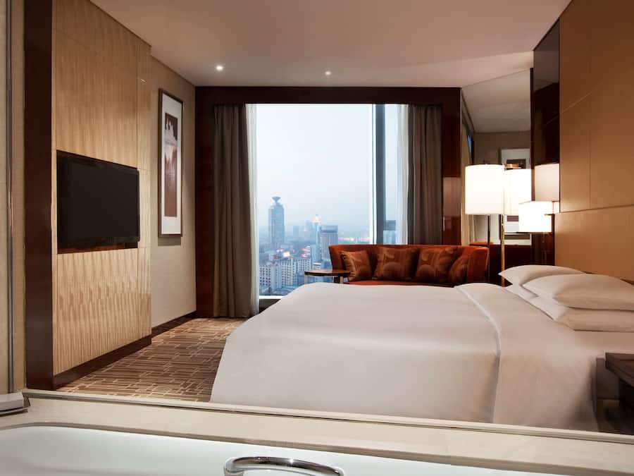 Una habitación de hotel con una cama grande, un sofá, una televisión y vistas a la ciudad.