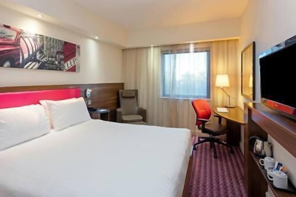 A hotel room with a bed, a desk, a chair, a TV, and a window with curtains.