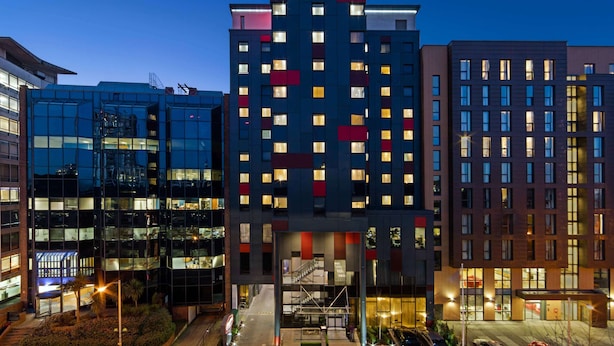 Un hôtel moderne, reconnaissable à son grand panneau « Hampton », qui s’étend sur plusieurs étages et possède une façade en verre.