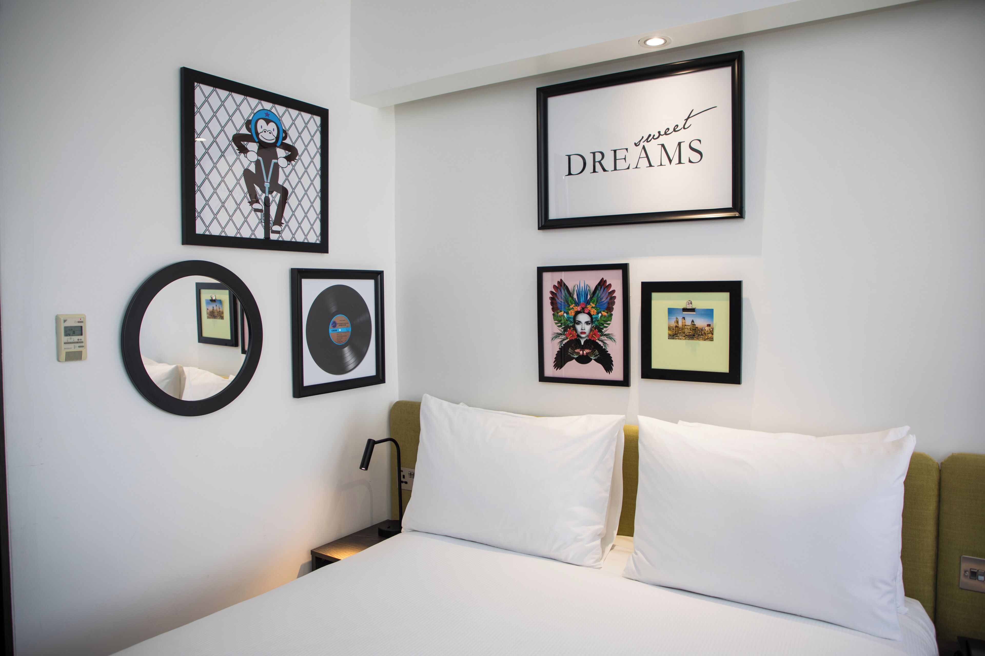 A hotel room with a bed, a bedside table, a lamp, and wall art including a framed picture with the text 'sweet DREAMS' and other framed artworks.