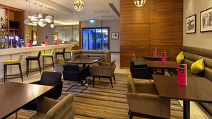 Un hall d’hôtel moderne doté d’un bar, de différents espaces aménagés pour s’asseoir et d’un grand mur revêtu de panneaux en bois.