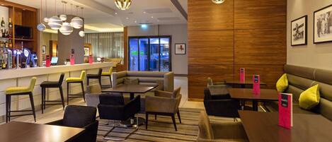 A modern hotel lobby with a bar area, seating arrangements, and a large wooden panel wall.