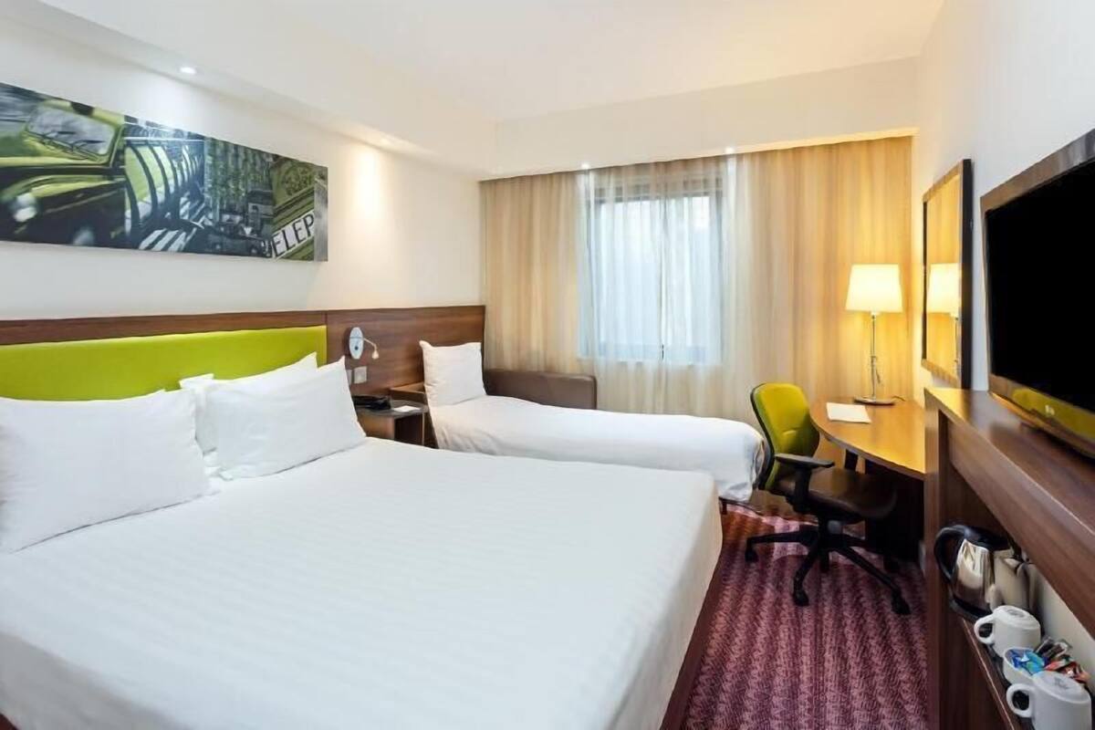 A hotel room with two beds, a desk, a chair, a television, and a painting on the wall.