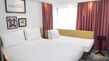 Une chambre d’hôtel avec un grand lit, deux tables de chevet, une commode, un tableau encadré au mur et une fenêtre avec des rideaux.