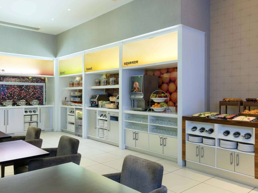 Cocina moderna con armarios blancos, comedor con mesa y sillas, y una exhibición de frutas.