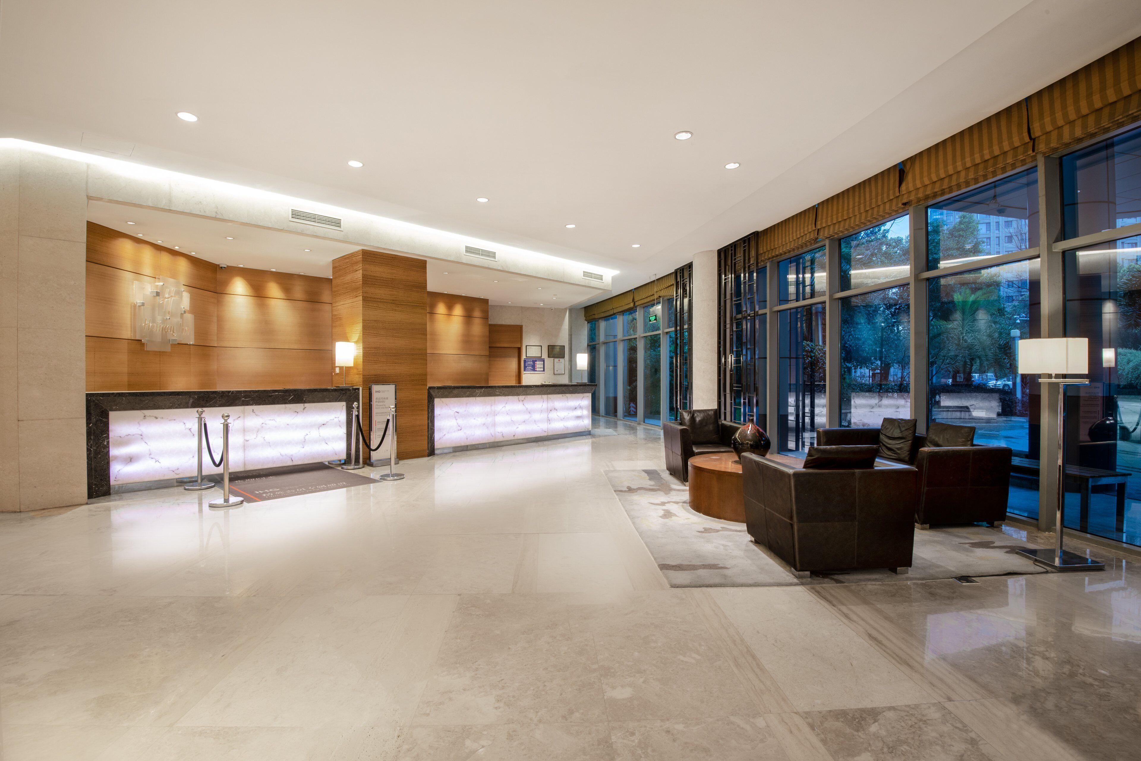 A spacious lobby with a reception desk, seating area, and large windows offering a view of the outdoors.