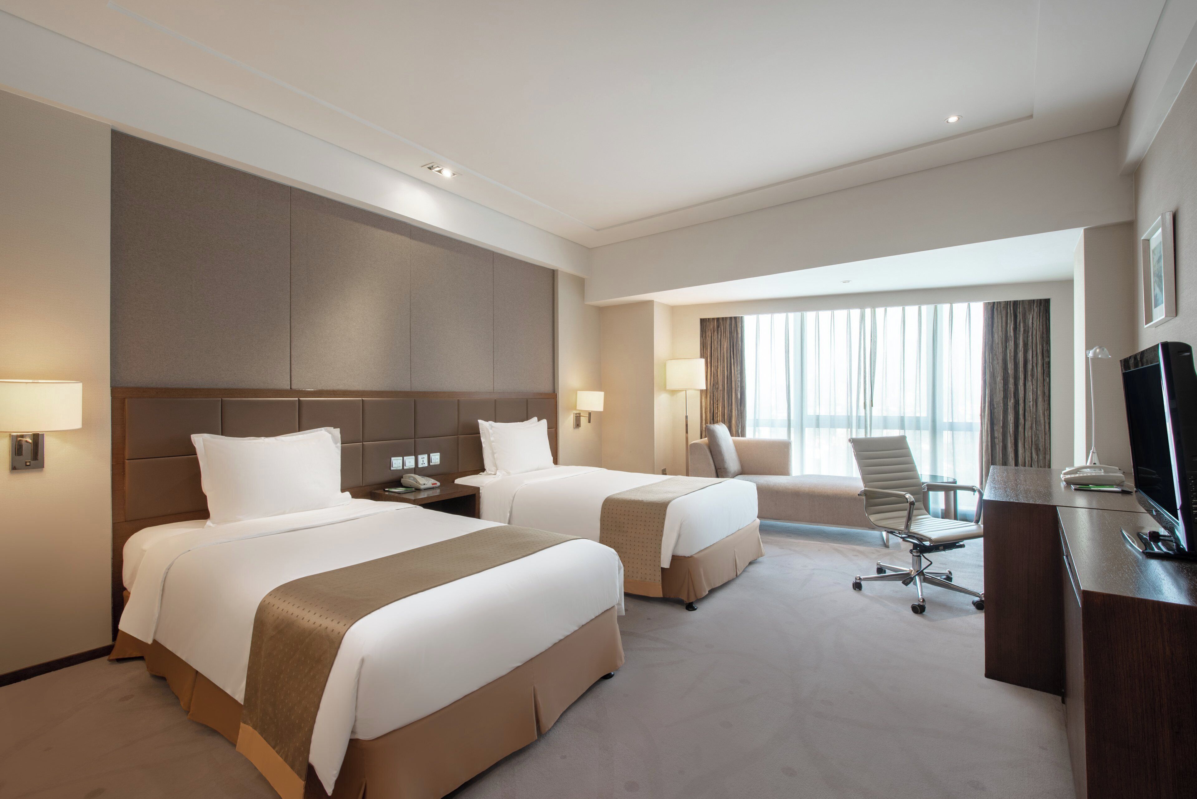 Ein Hotelzimmer mit zwei Betten, einem Schreibtisch, einem Stuhl und einem Fernseher.