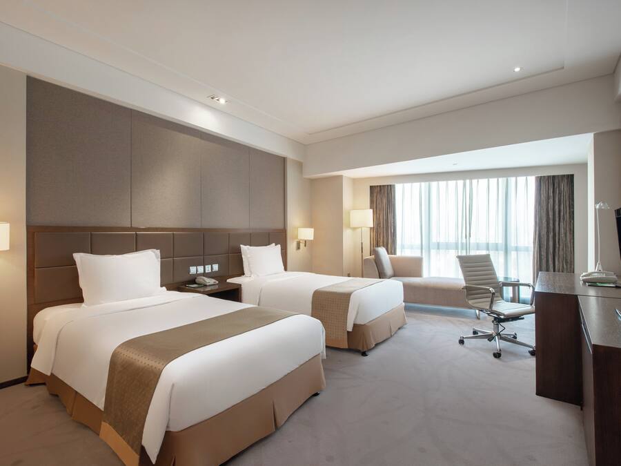 Ein Hotelzimmer mit zwei Betten, einem Schreibtisch, einem Stuhl und einem Fernseher.