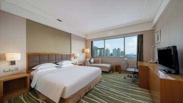 Habitación de hotel con una cama grande, un escritorio con televisor y vistas a la ciudad.