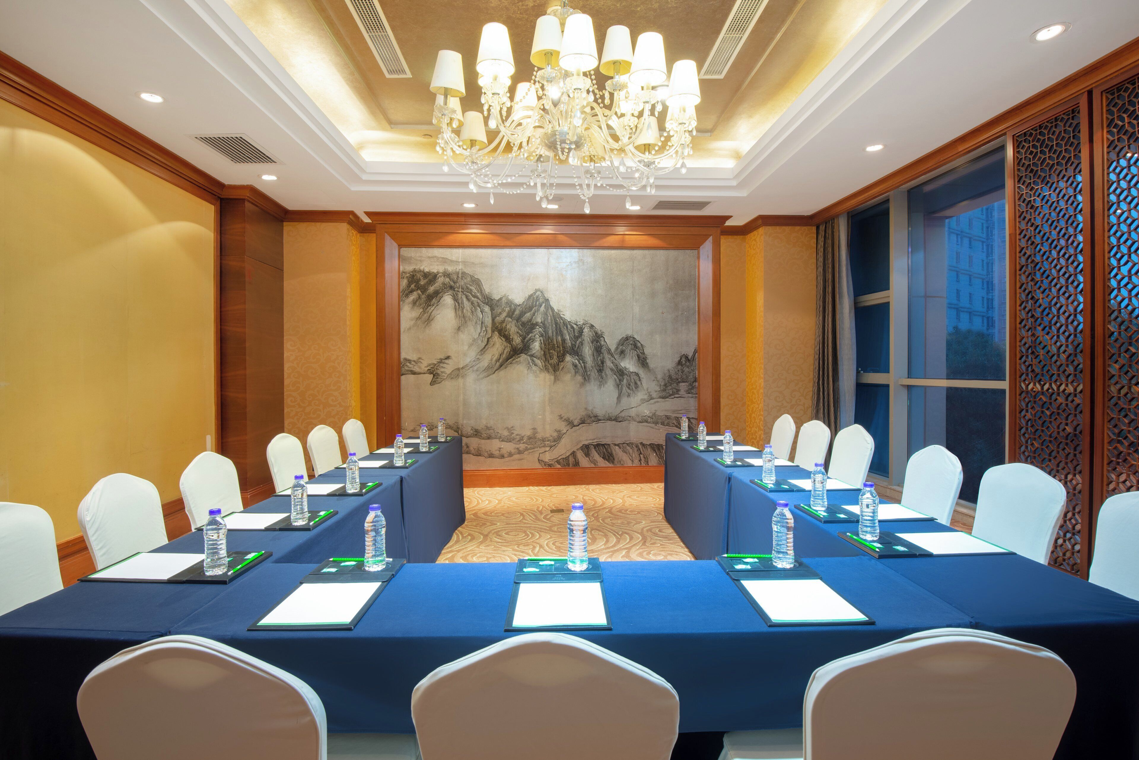 A conference room with a long table, white chairs, water bottles, and a large wall painting.