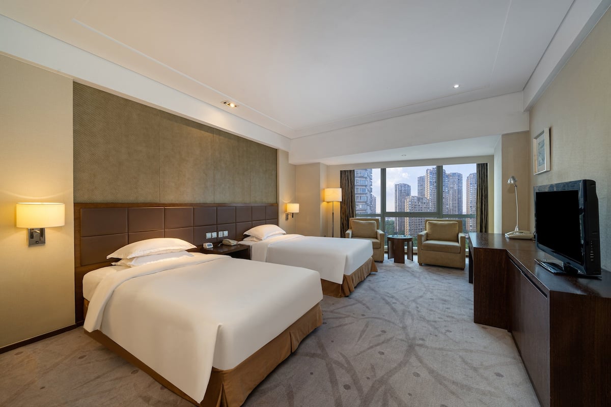 Ein Hotelzimmer mit zwei Betten, einem Schreibtisch, einem Fernseher und Blick auf die Stadt.