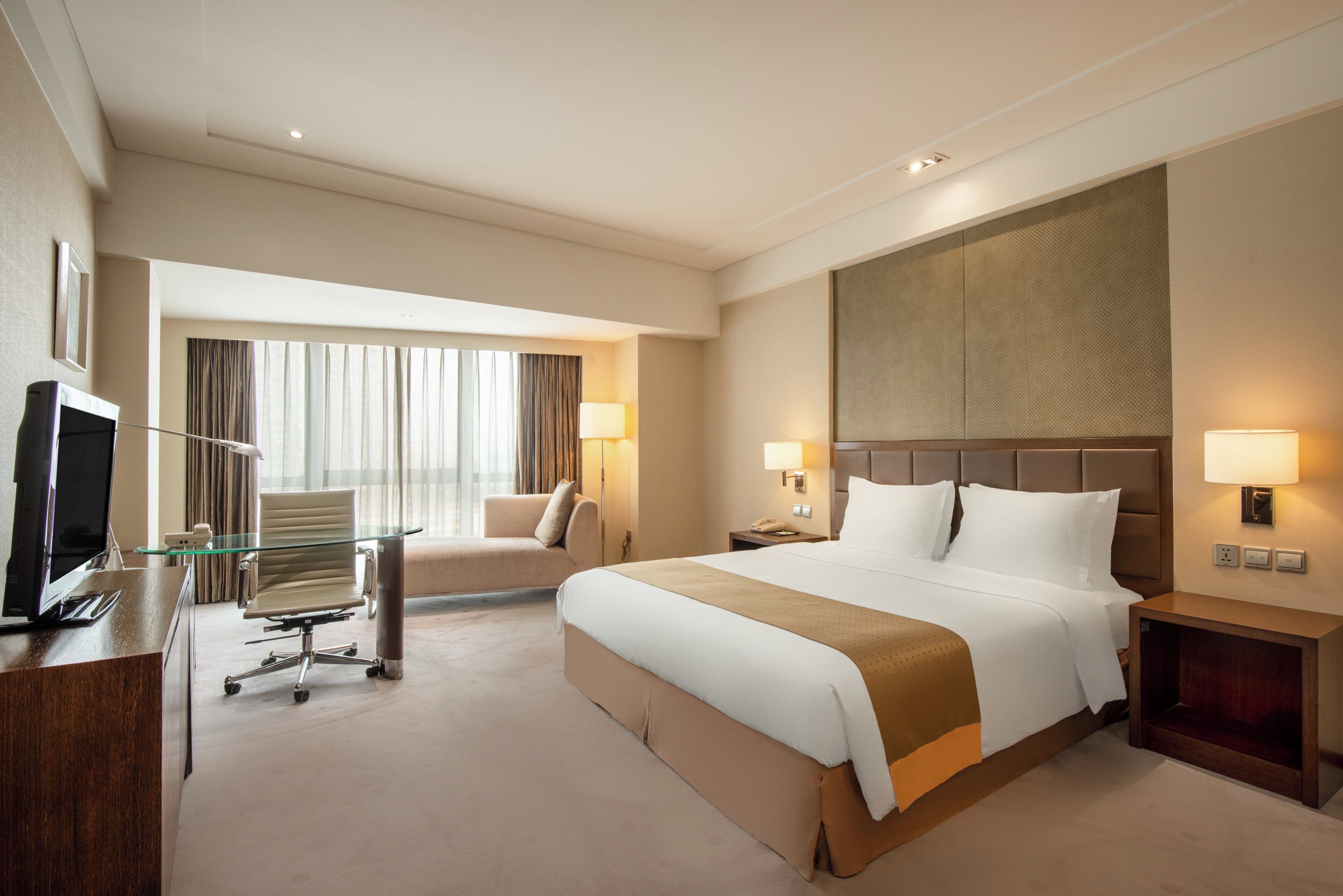 A hotel room with a bed, a desk with a computer, a chair, and a television.