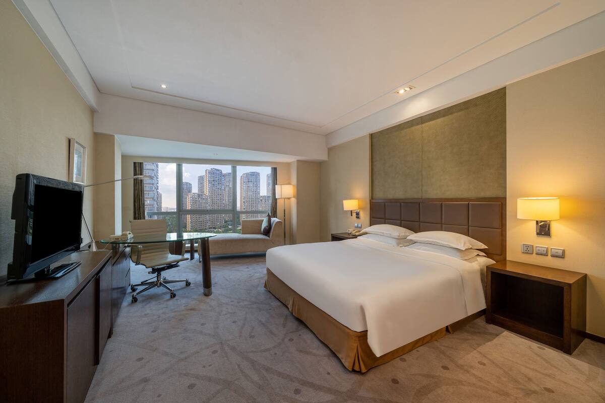 Ein Hotelzimmer mit Bett, Schreibtisch, Fernseher und Blick auf die Stadt.