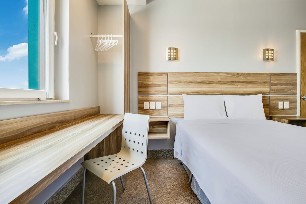 Ein Hotelzimmer mit Bett, Schreibtisch, Stuhl und einem Fenster mit Meerblick.