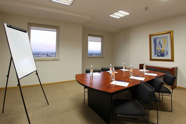 Un salón de conferencias con una gran mesa, sillas, una pizarra y ventanas con vista a la ciudad.