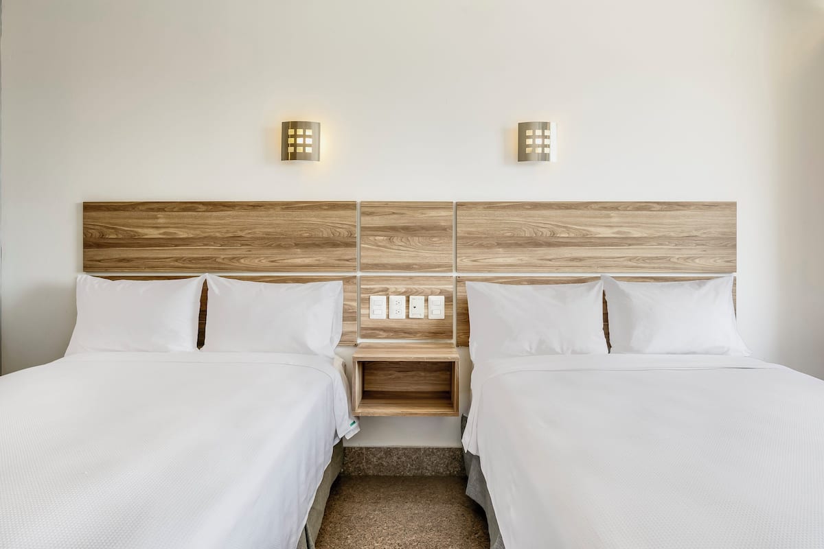 Ein Hotelzimmer mit zwei Betten, einem hölzernen Kopfteil, Nachttischen und Wandleuchten.