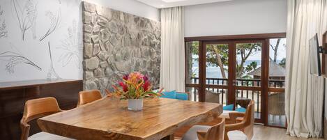 A dining area with a wooden table and chairs, a stone accent wall, and a view of the sea through large windows.