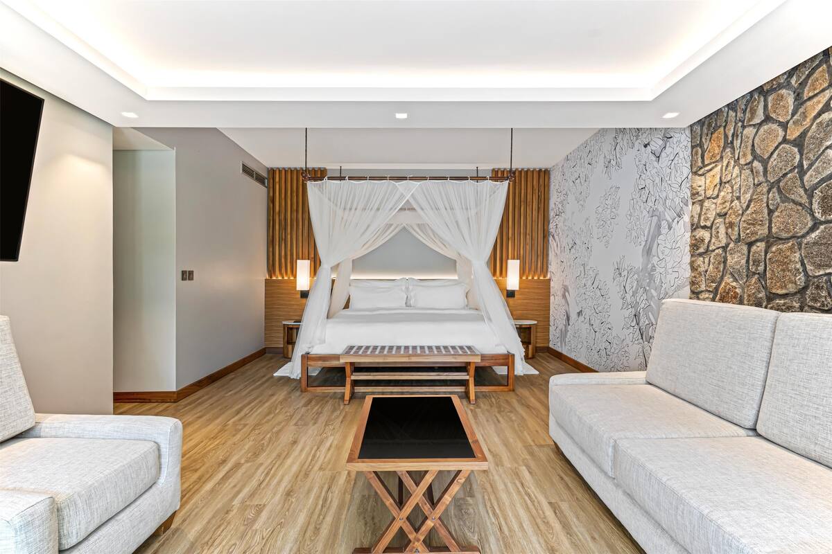 Un dormitorio moderno con cama con dosel, un sofá y una pared decorada con piedra.