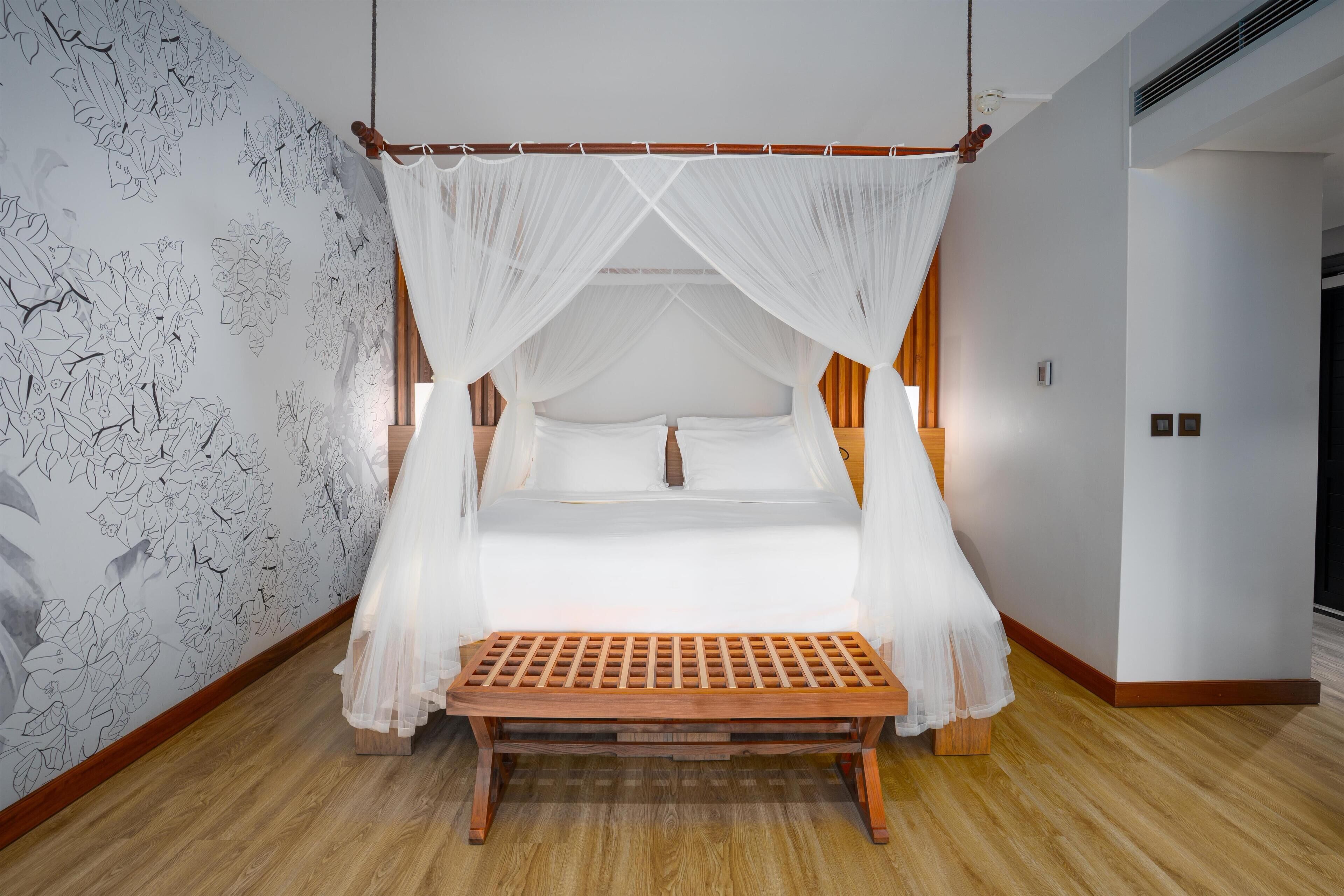 Quarto com cama de dossel, um banquinho de madeira e parede com padrão floral.