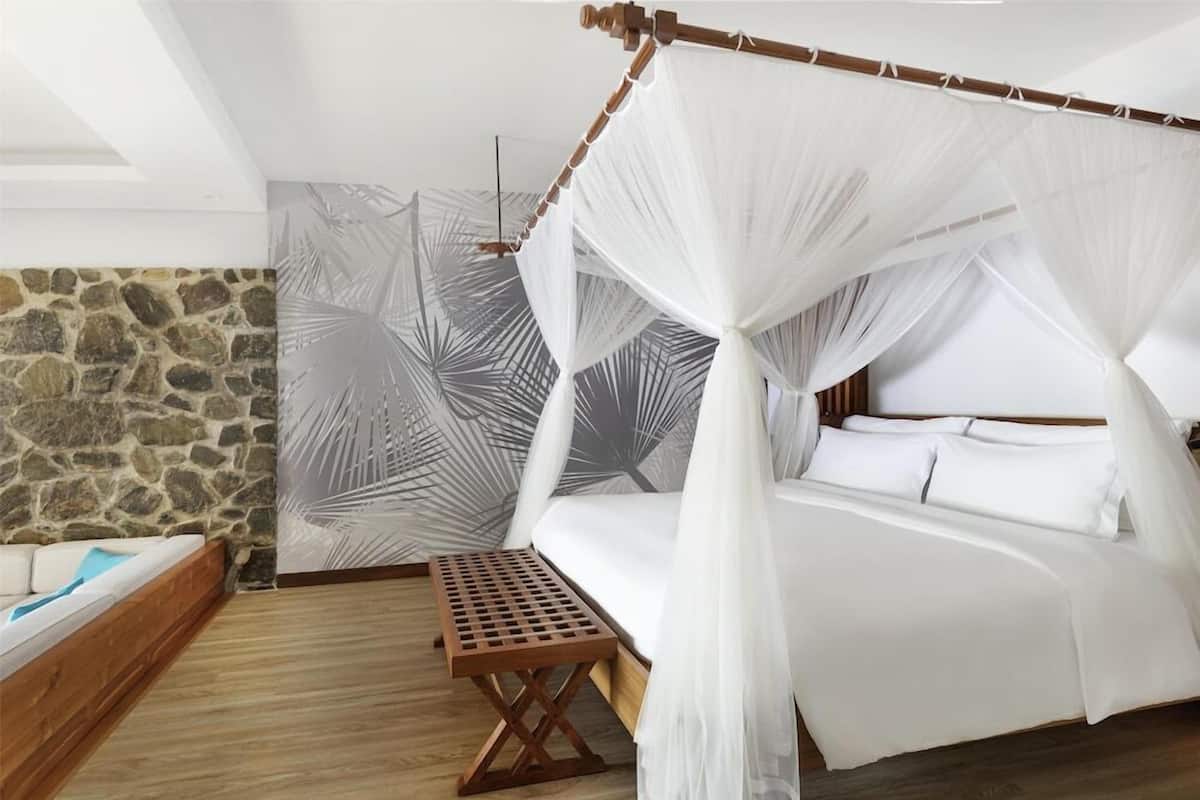Une chambre à coucher avec un lit à baldaquin, un mur en pierre et un papier peint à motifs de feuilles de palmier.