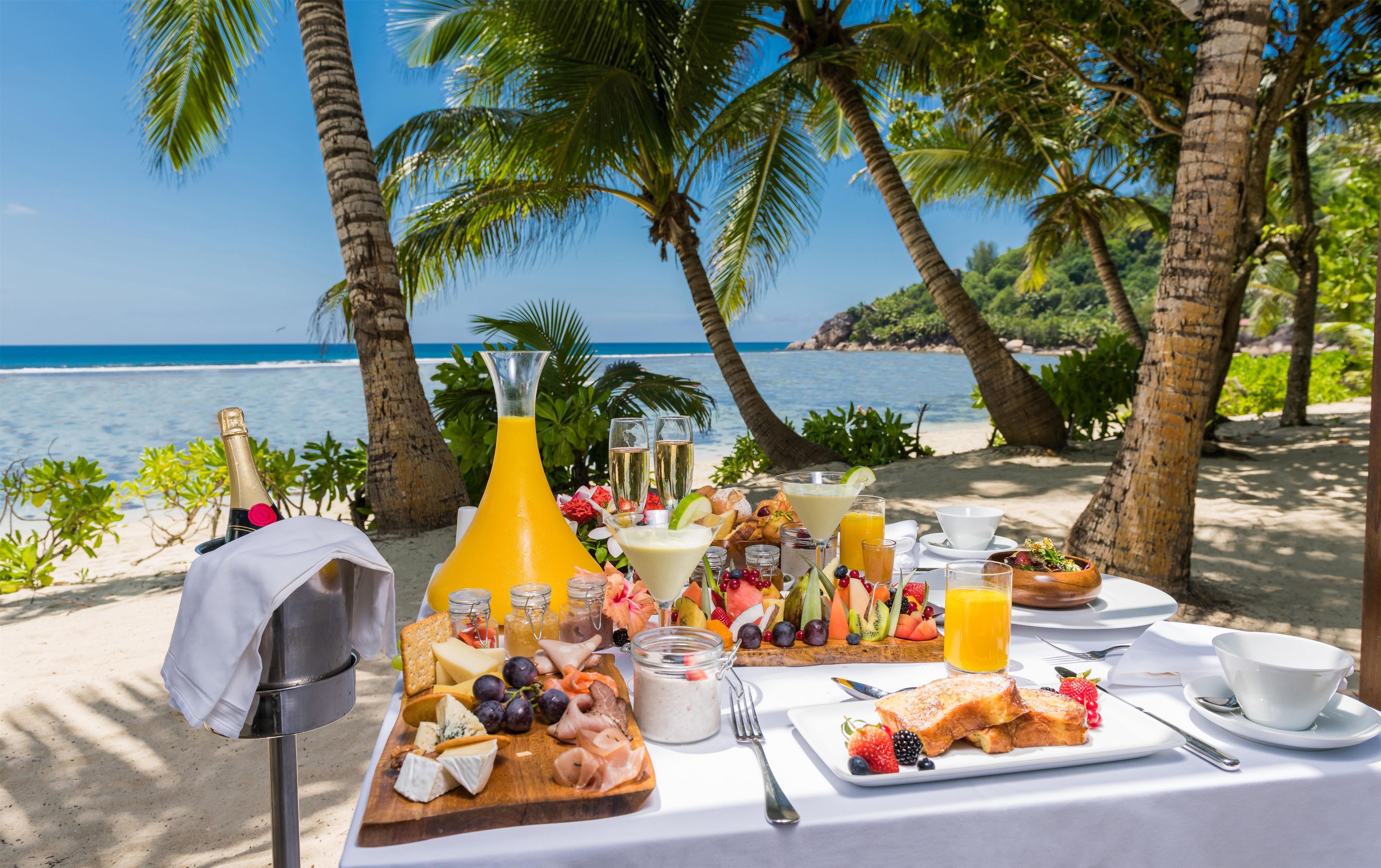 Un buffet de petit-déjeuner installé sur une plage, avec vue sur l’océan, comprenant une variété de plats et de boissons.