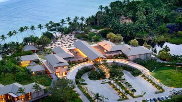 Un resort con varias edificaciones, un estacionamiento y una playa con sombrillas.