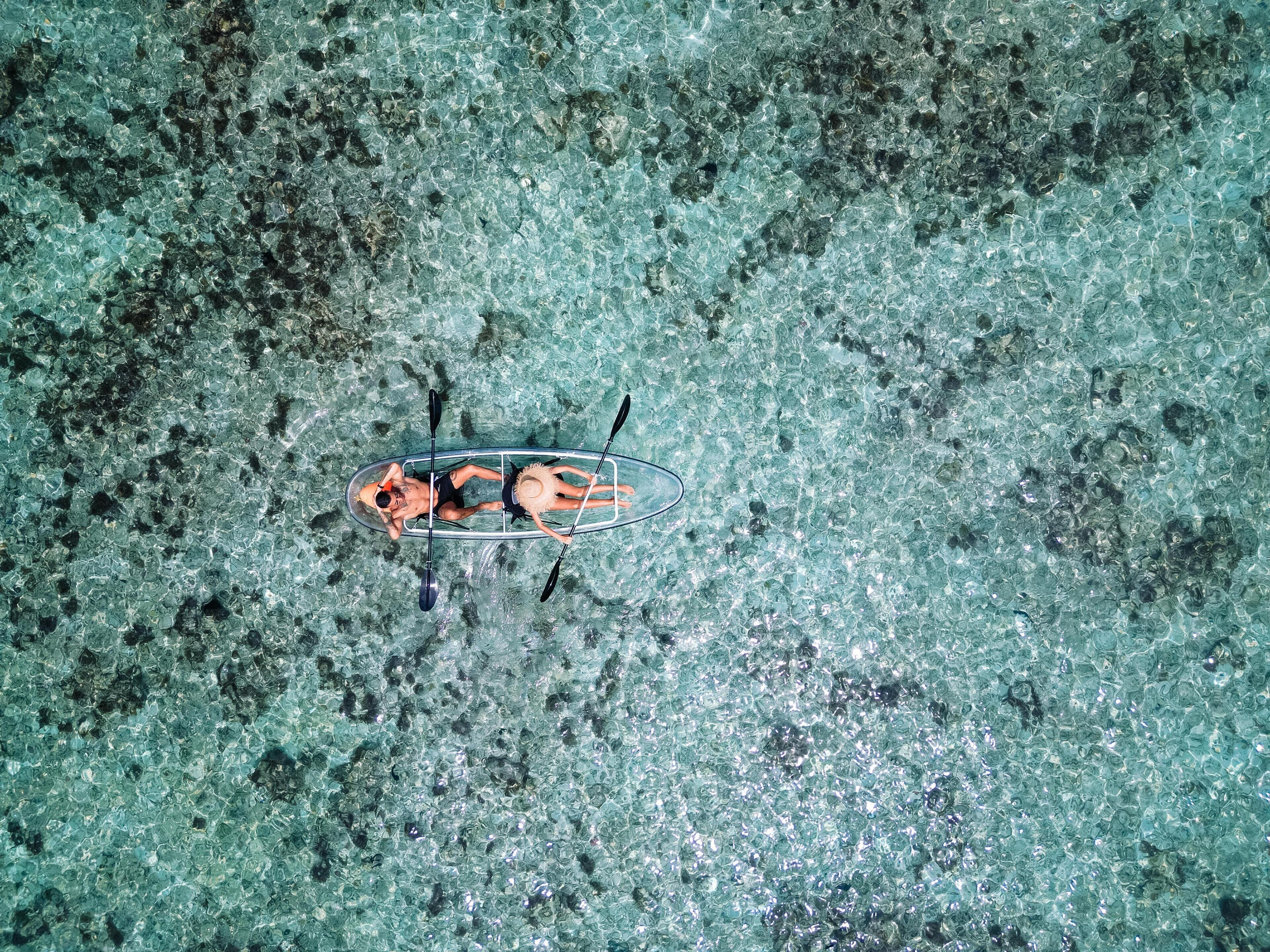 An aerial view of a clear blue water body with a small boat containing two people.