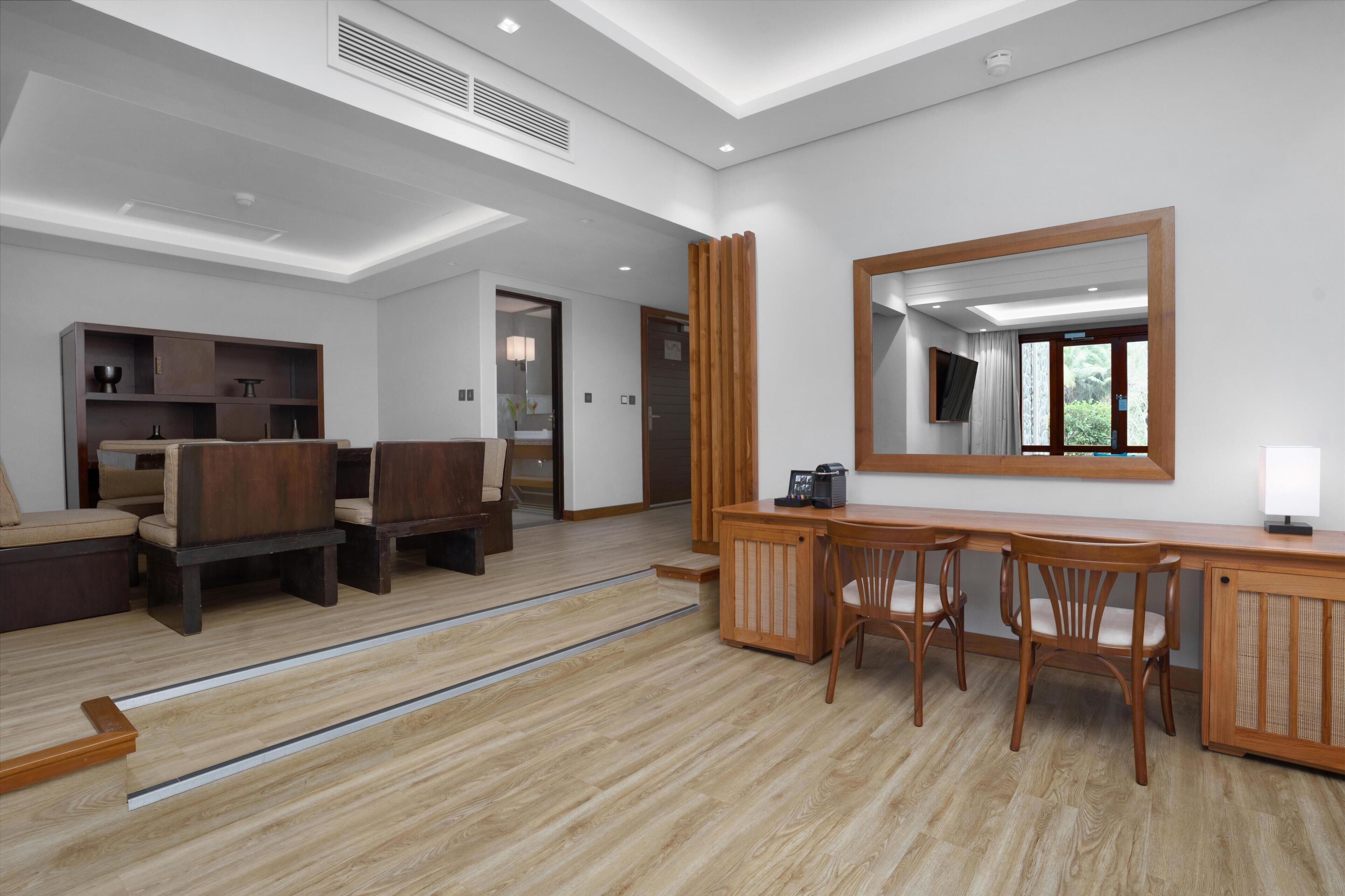 Una sala de estar moderna con un banco de madera, una zona de comedor con una mesa y sillas de madera, un espejo grande y un mueble empotrado.