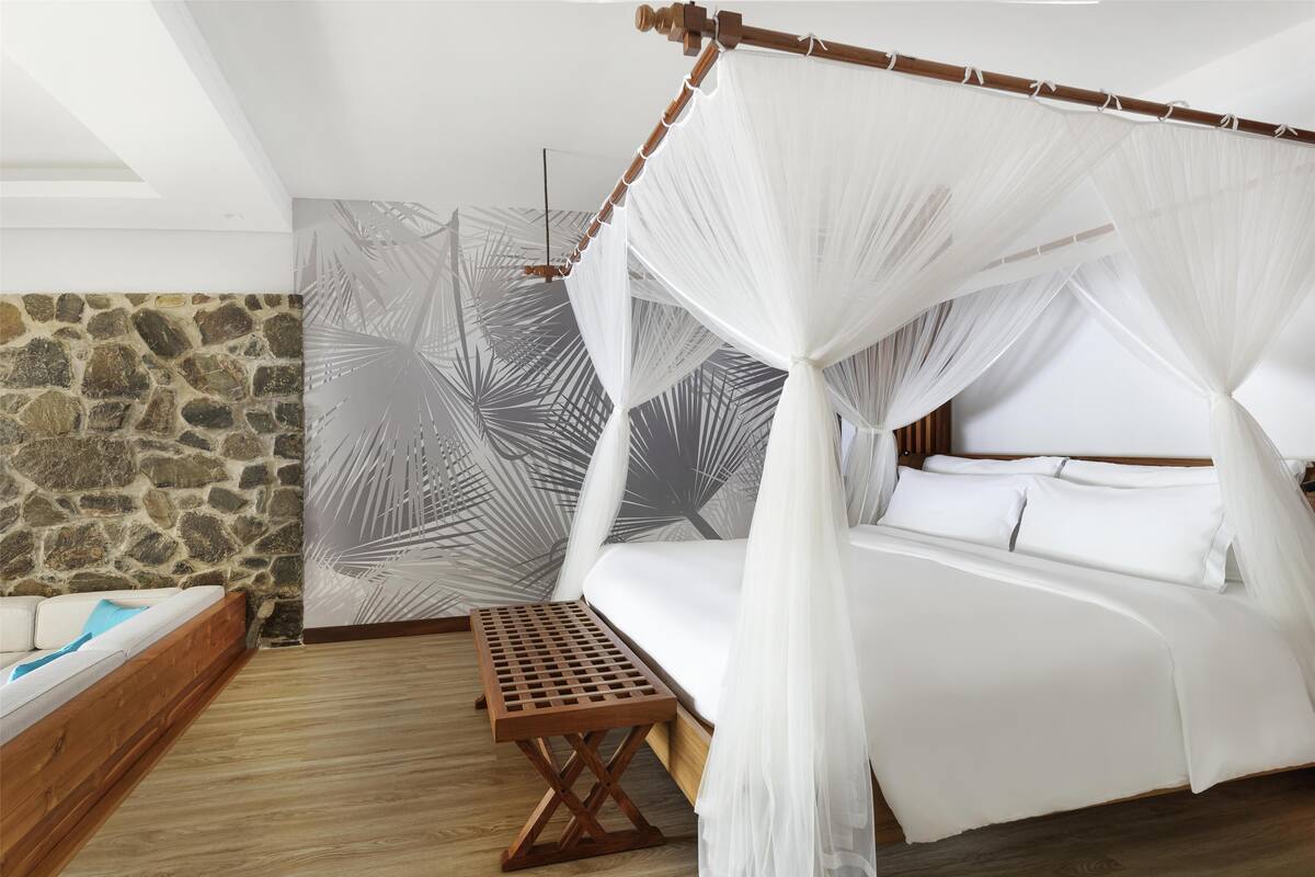 Ein Schlafzimmer mit einem Baldachinbett, einer hölzernen Bank, einer Steinwand und einem großen Wandgemälde mit Blattmuster.