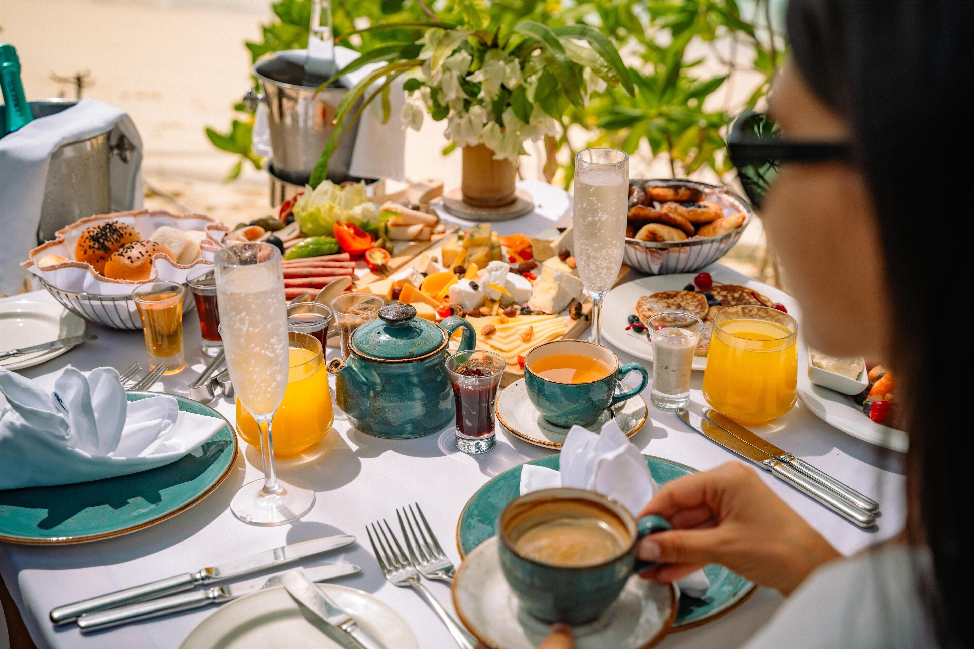 A table set with breakfast items including fruits, cheeses, and pastries, along with drinks and a teapot.