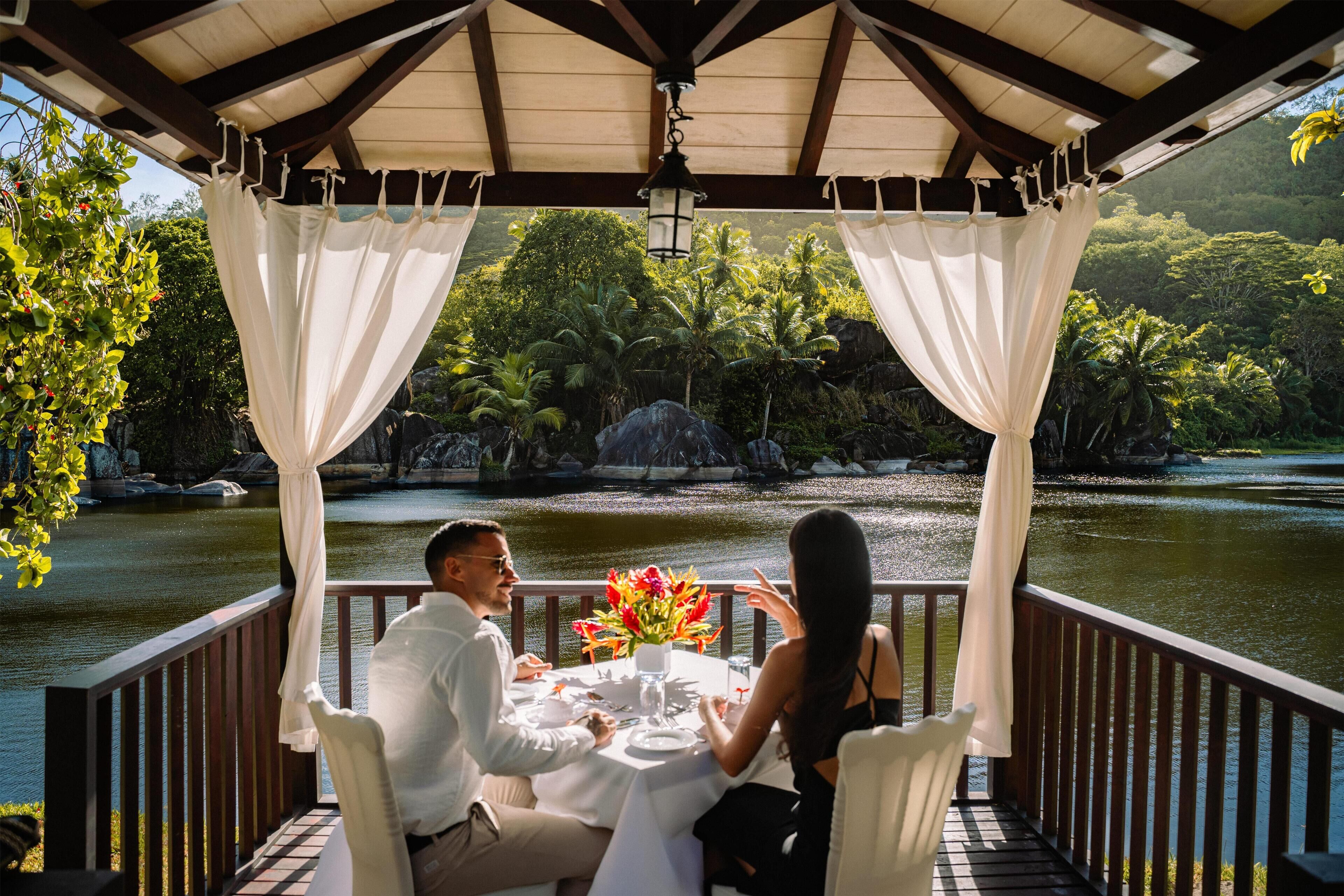Un couple est assis à une table, devant un paysage tropical et avec vue sur un lac.