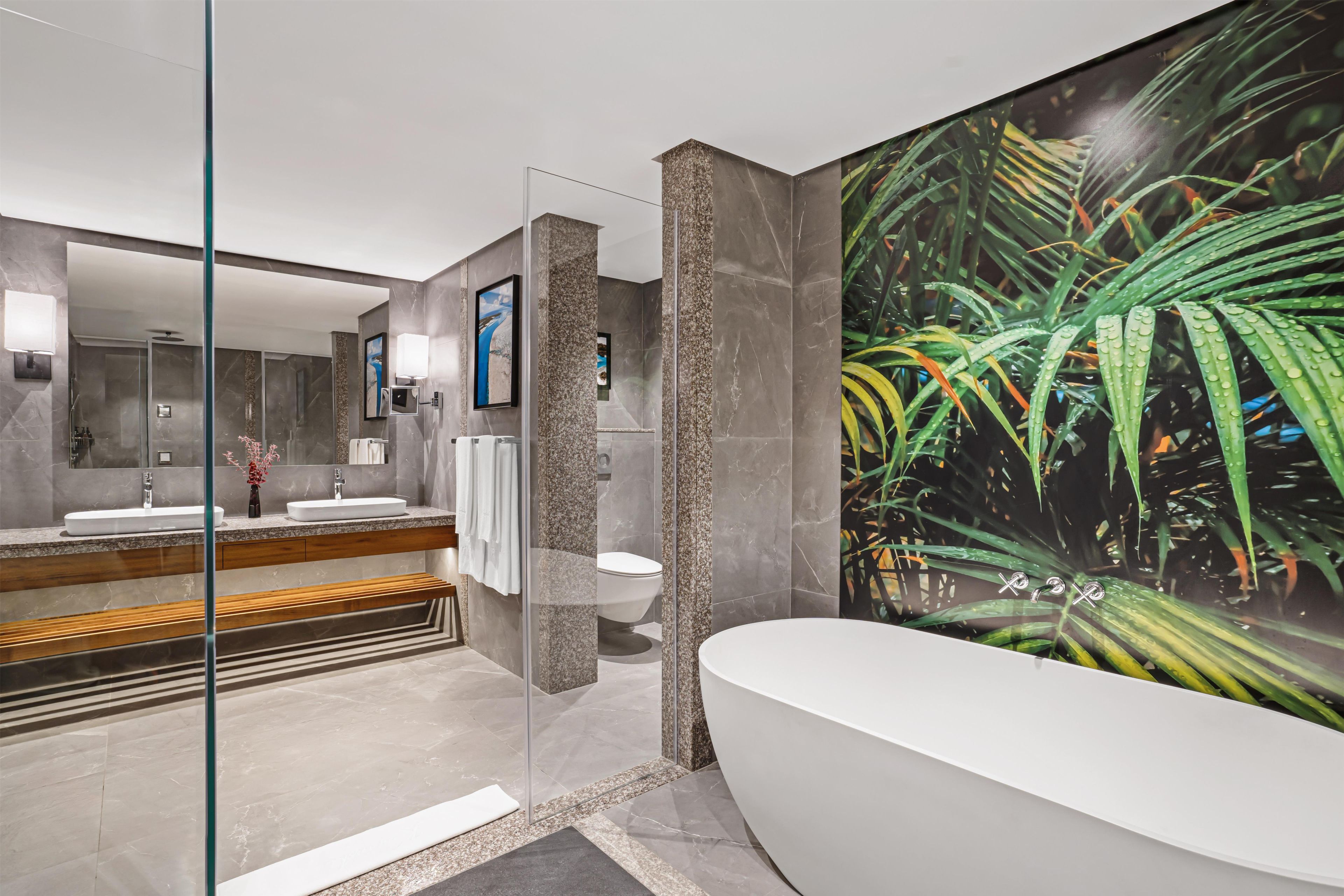 Un baño moderno con una bañera independiente, ducha con mampara de vidrio y un espejo grande.