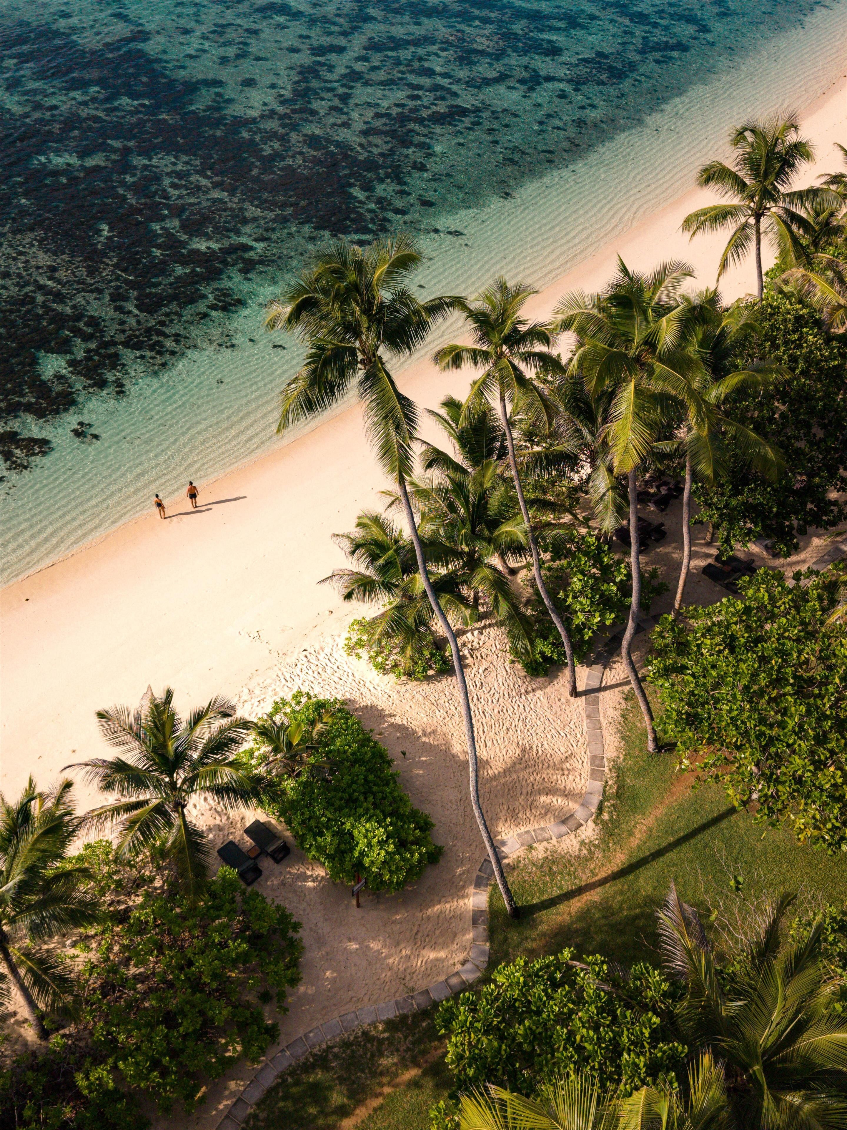 Luchtbeeld van een strand met helder turquoise water, een zandstrand en palmbomen.