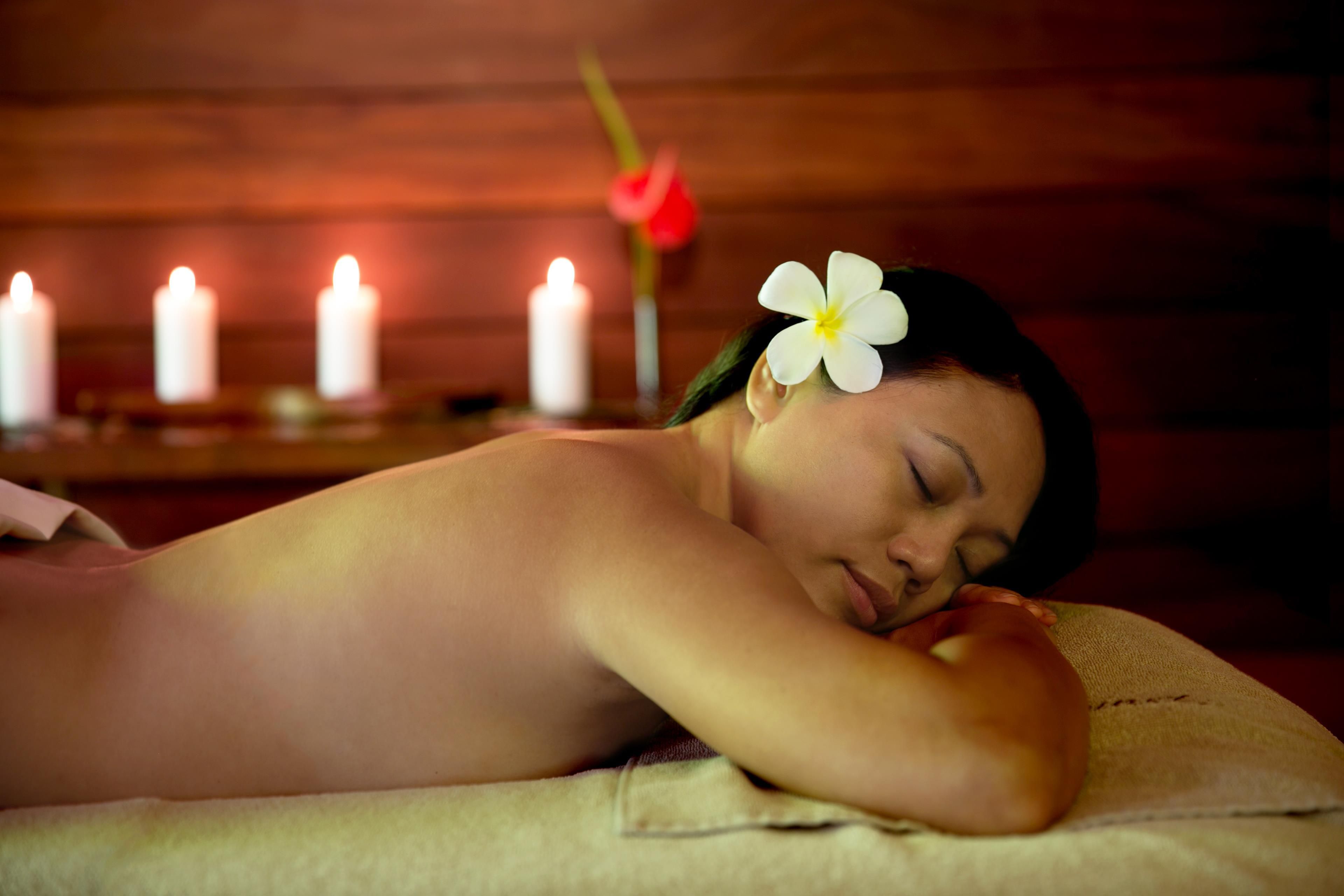 A person lying on a massage table with candles in the background.