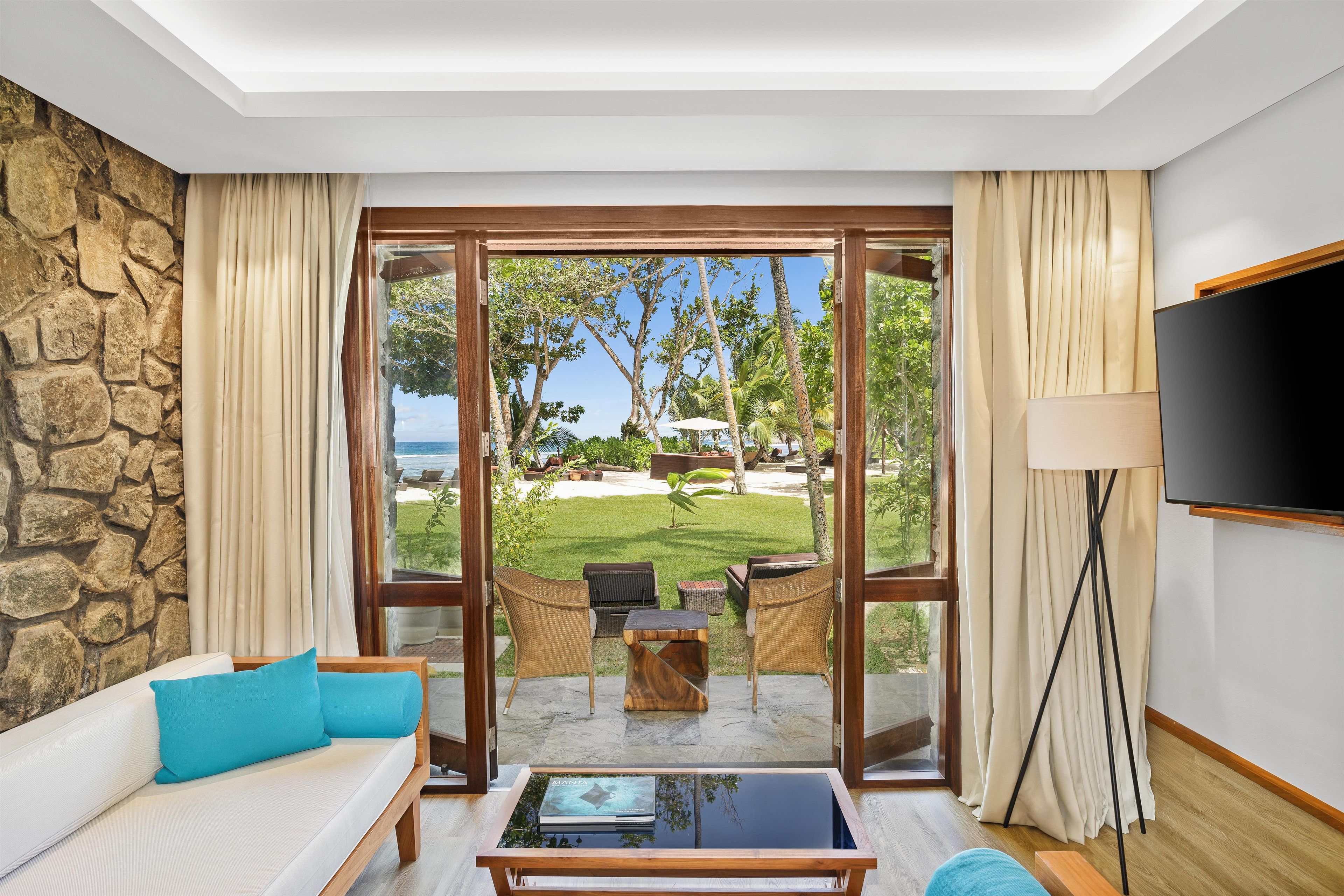 Habitación de hotel con sofá, mesa de centro, televisor y vistas a un jardín y al océano.