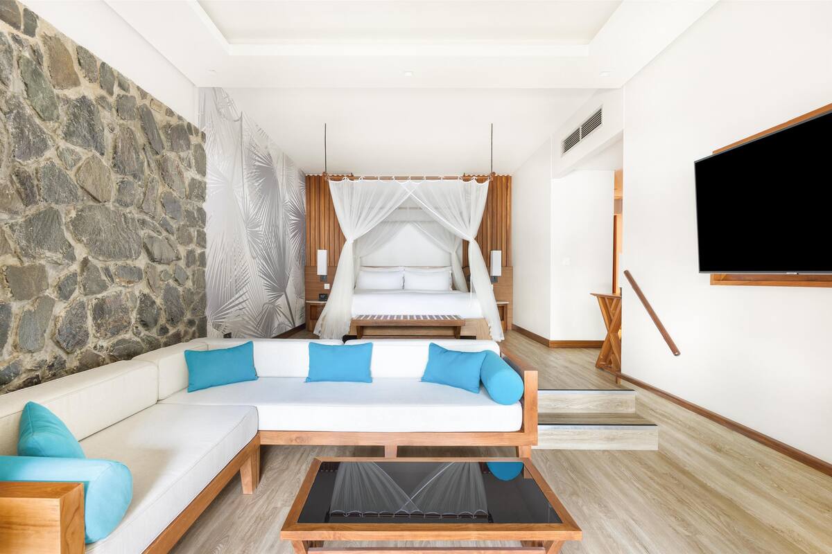 Un dormitorio moderno con pared de piedra, cama con dosel, sofá con cojines azules y televisor montado en la pared.