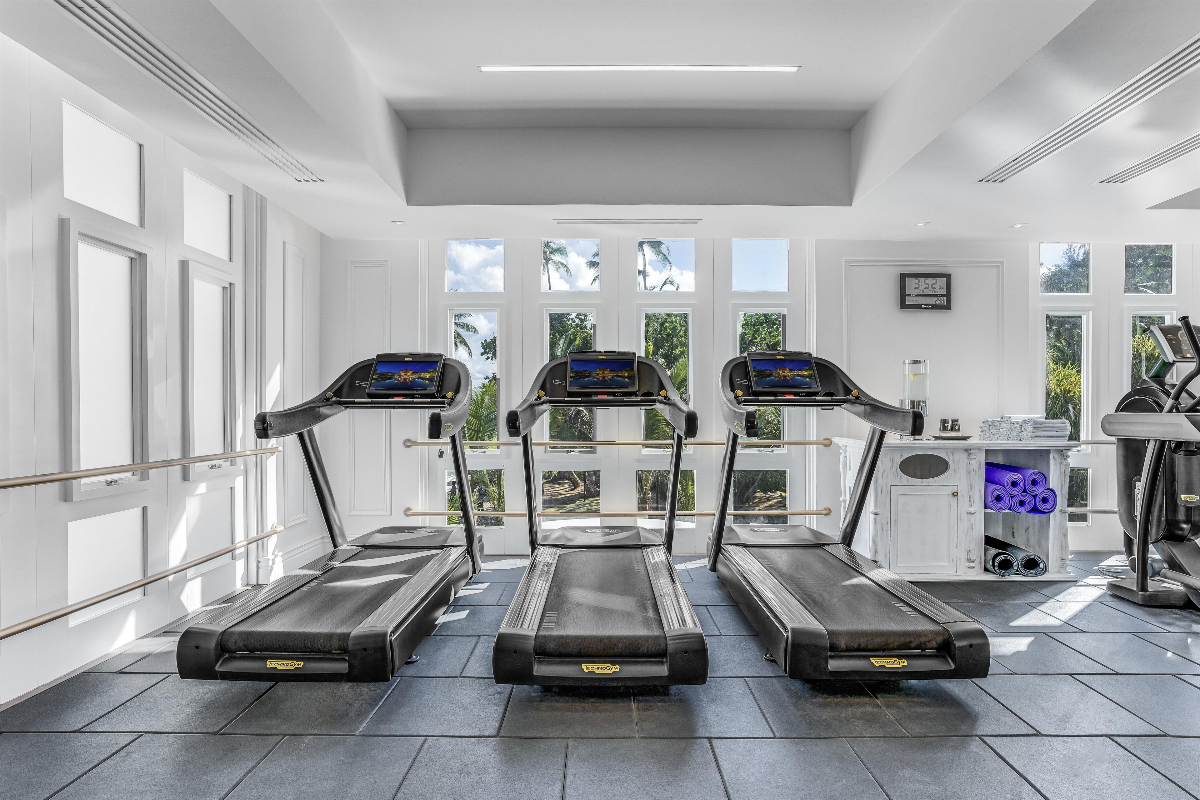 A gym with three treadmills, a water station, and a digital clock on the wall.