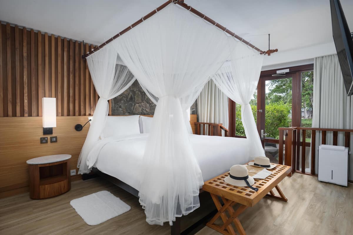 Ein Schlafzimmer mit einem Himmelsbett, einem Nachttisch mit Hüten, einem kleinen runden Tisch und einer weißen Heizung.