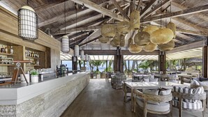 A spacious bar area with a long counter, wooden chairs, and hanging woven light fixtures. - Kempinski Seychelles Resort (Mahé Island)