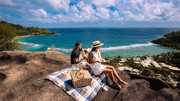 A couple on a blanket overlooking a beach with a clear view of the ocean and a resort in the background.