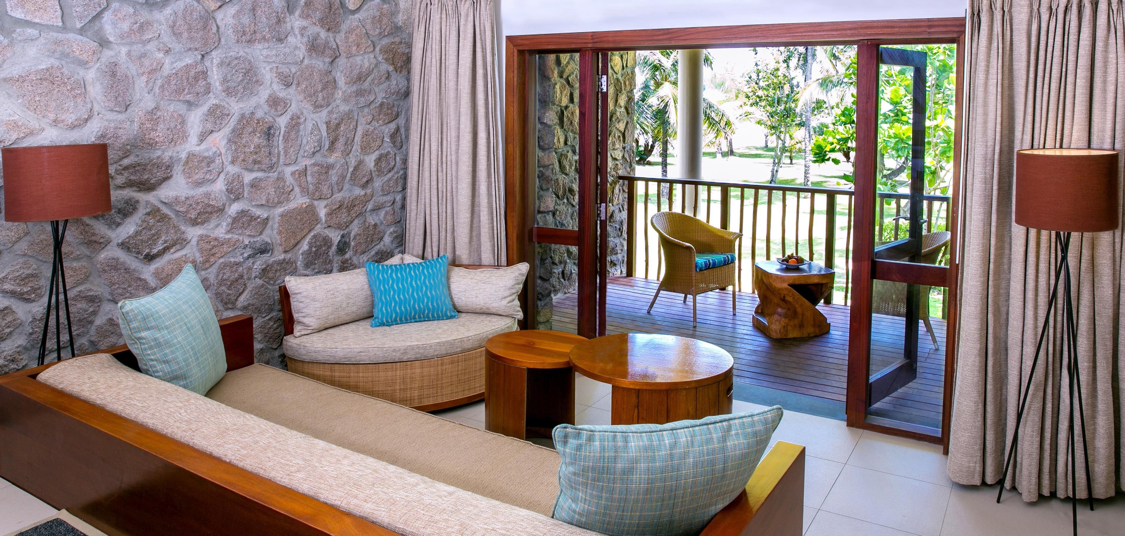 Una habitación con pared de piedra, un sofá, una mesita y un balcón con una silla y una mesa.