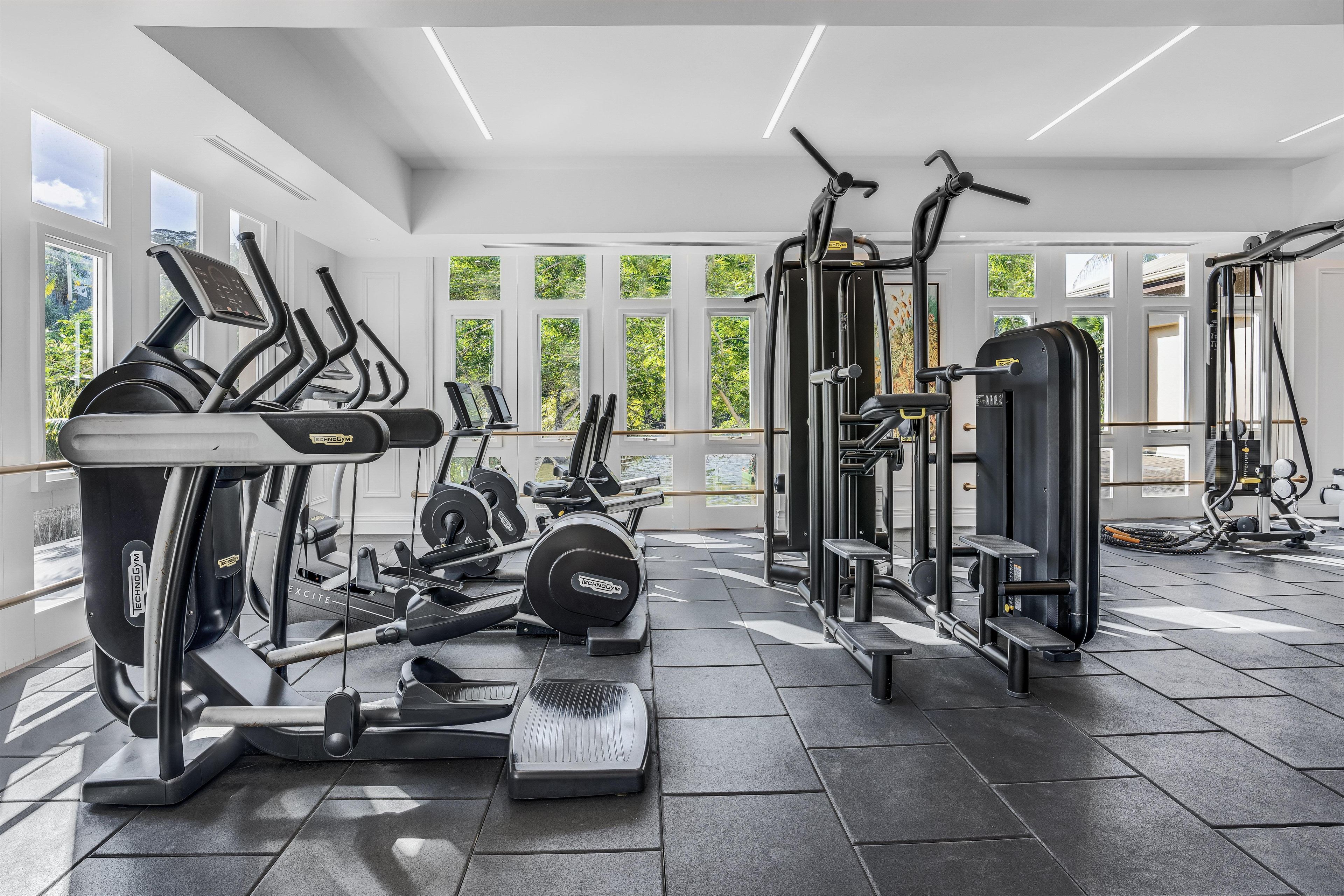 A modern gym with various exercise equipment, large windows, and a clean, spacious layout.