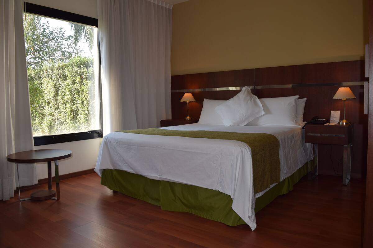 Een hotelkamer met een bed, twee nachtkastjes, een klein rond tafeltje en een raam met gordijnen.