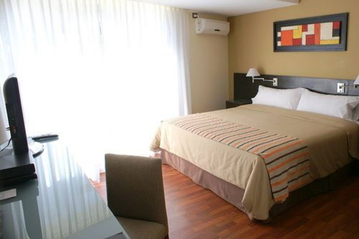 Een hotelkamer met een bed, een bureau, een stoel en een raam met gordijnen.