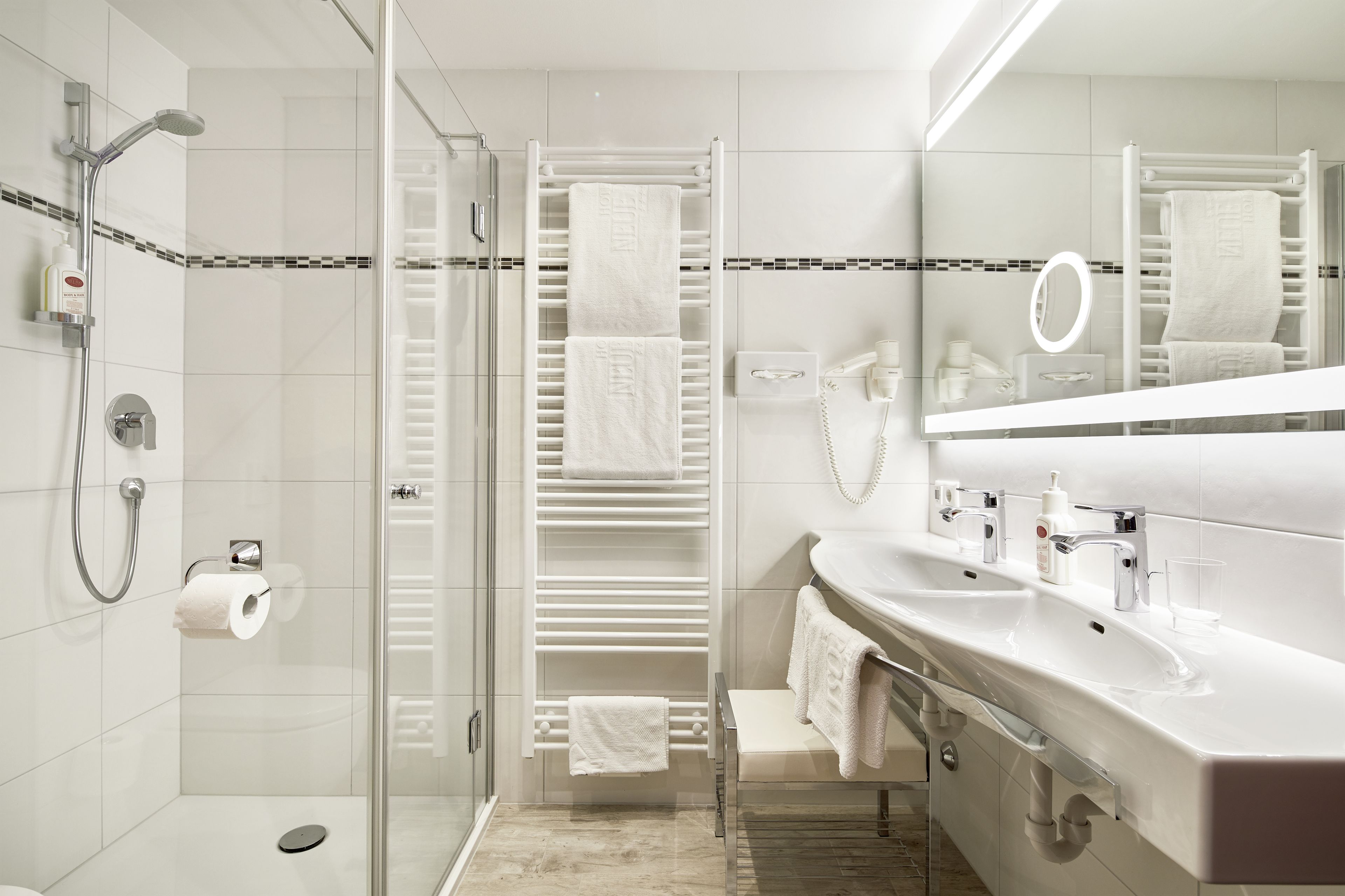 Un baño moderno con cabina de ducha de vidrio, toallero blanco, tocador con espejo y lavamanos.
