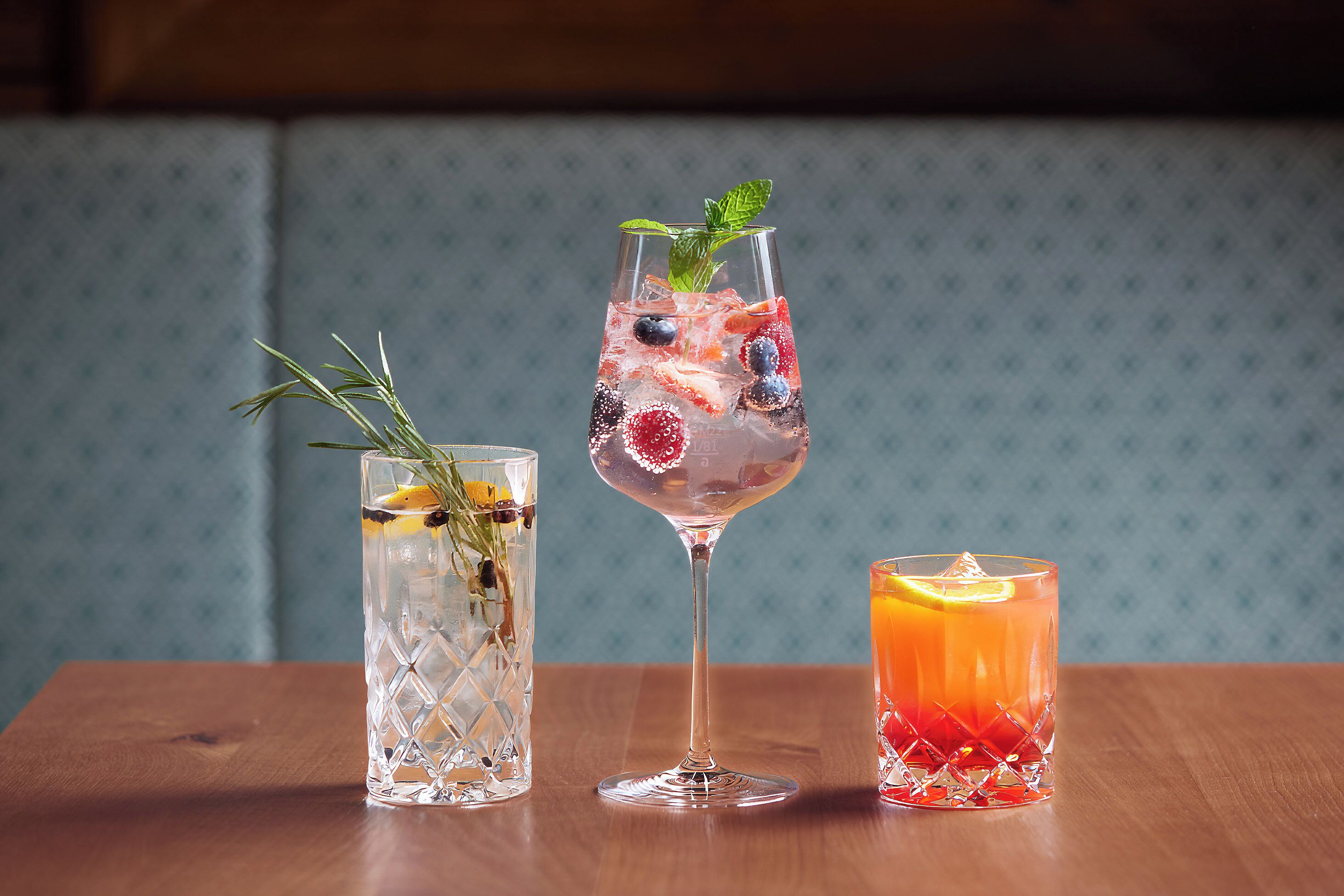 Three glasses of beverages on a wooden table against a patterned wall.