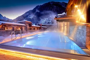 A heated outdoor pool with stone walls and a mountainous backdrop. - Hotel Neue Post (Mayrhofen)