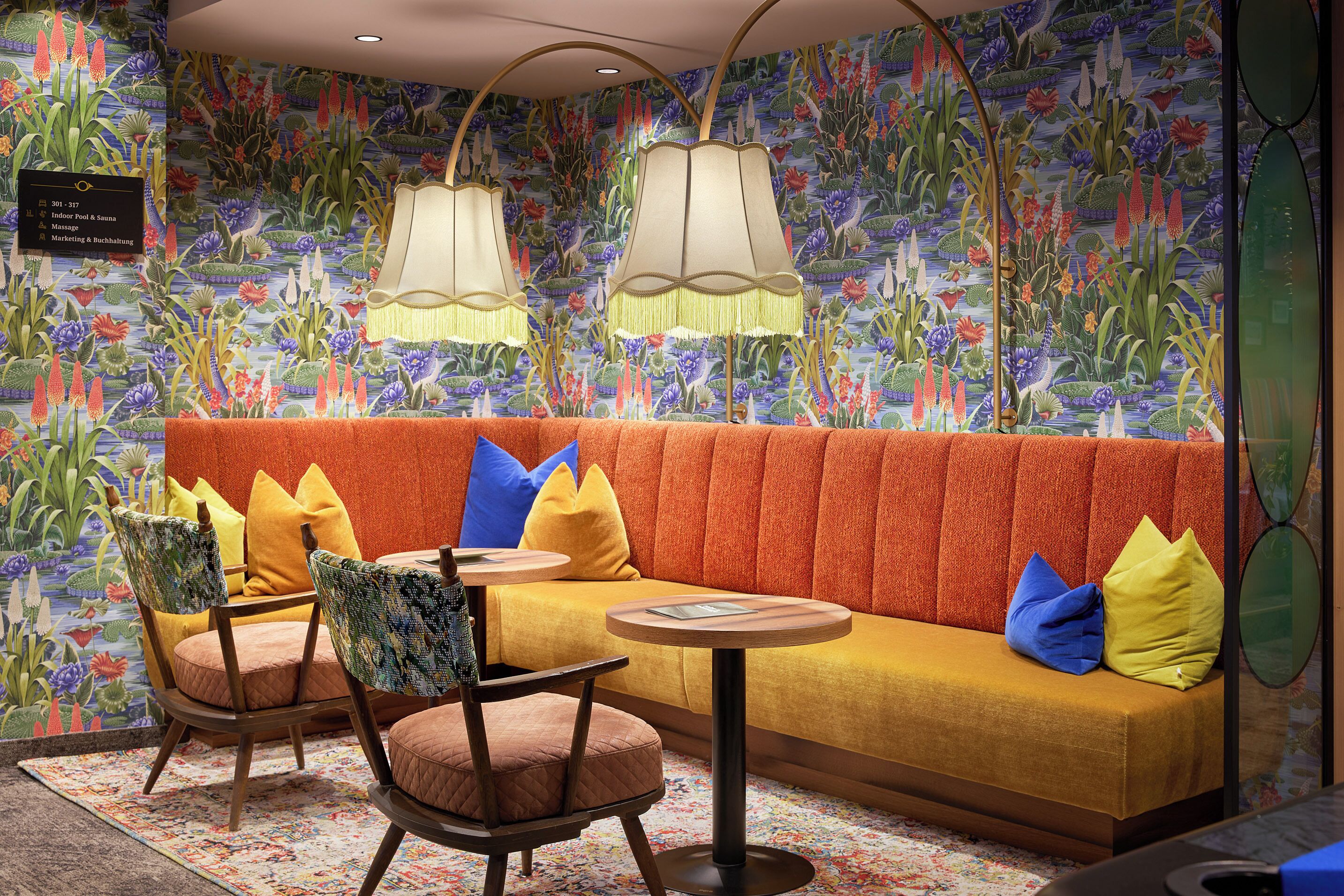 A room with a sofa, chairs, a small table, and a wall with a floral mural.